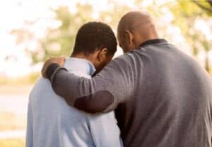 A person consoling another with their arm around their shoulder.